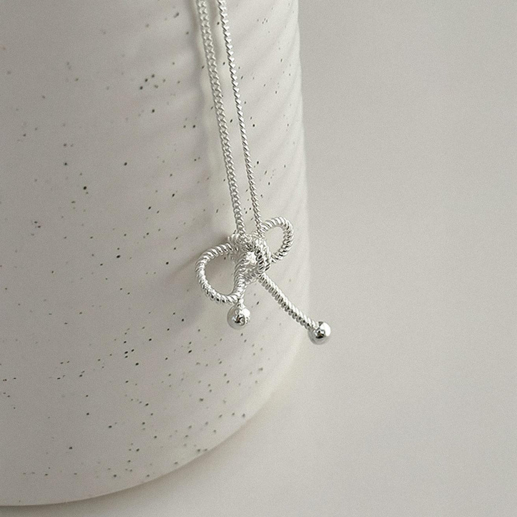 Sterling silver rope bow pendant necklace displayed on a ceramic mug