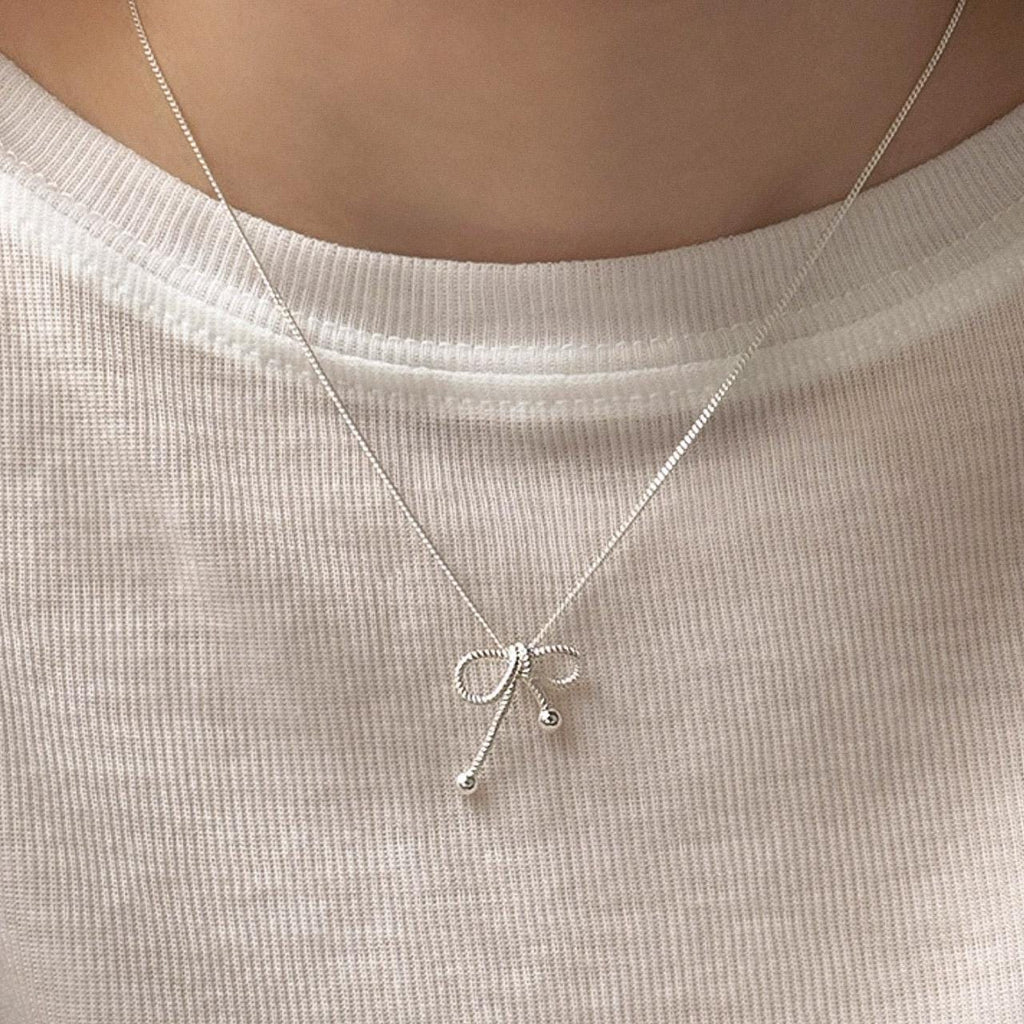 Woman wearing a sterling silver rope bow pendant necklace with a minimalist design