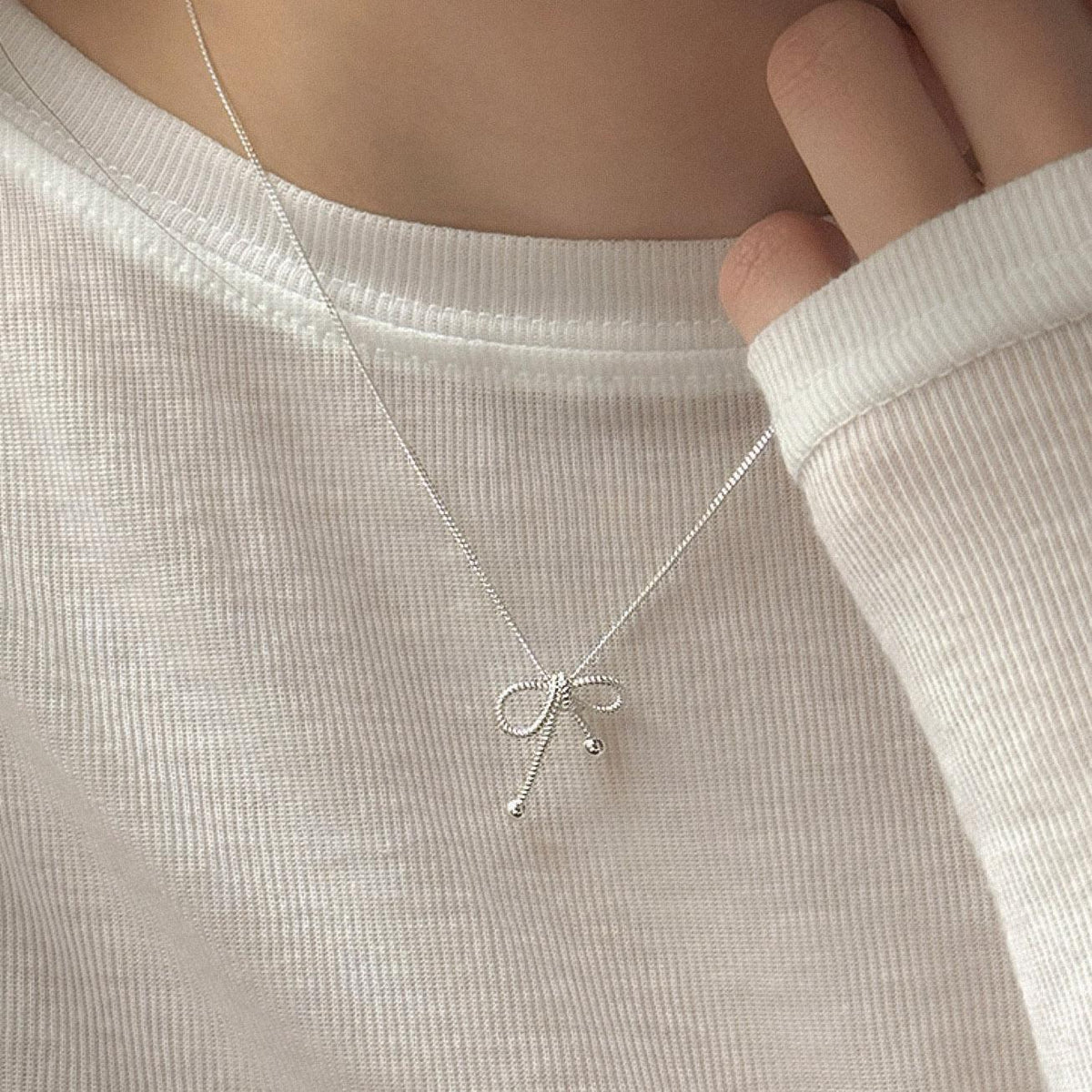Close-up of a sterling silver rope bow pendant necklace styled with a white knit top