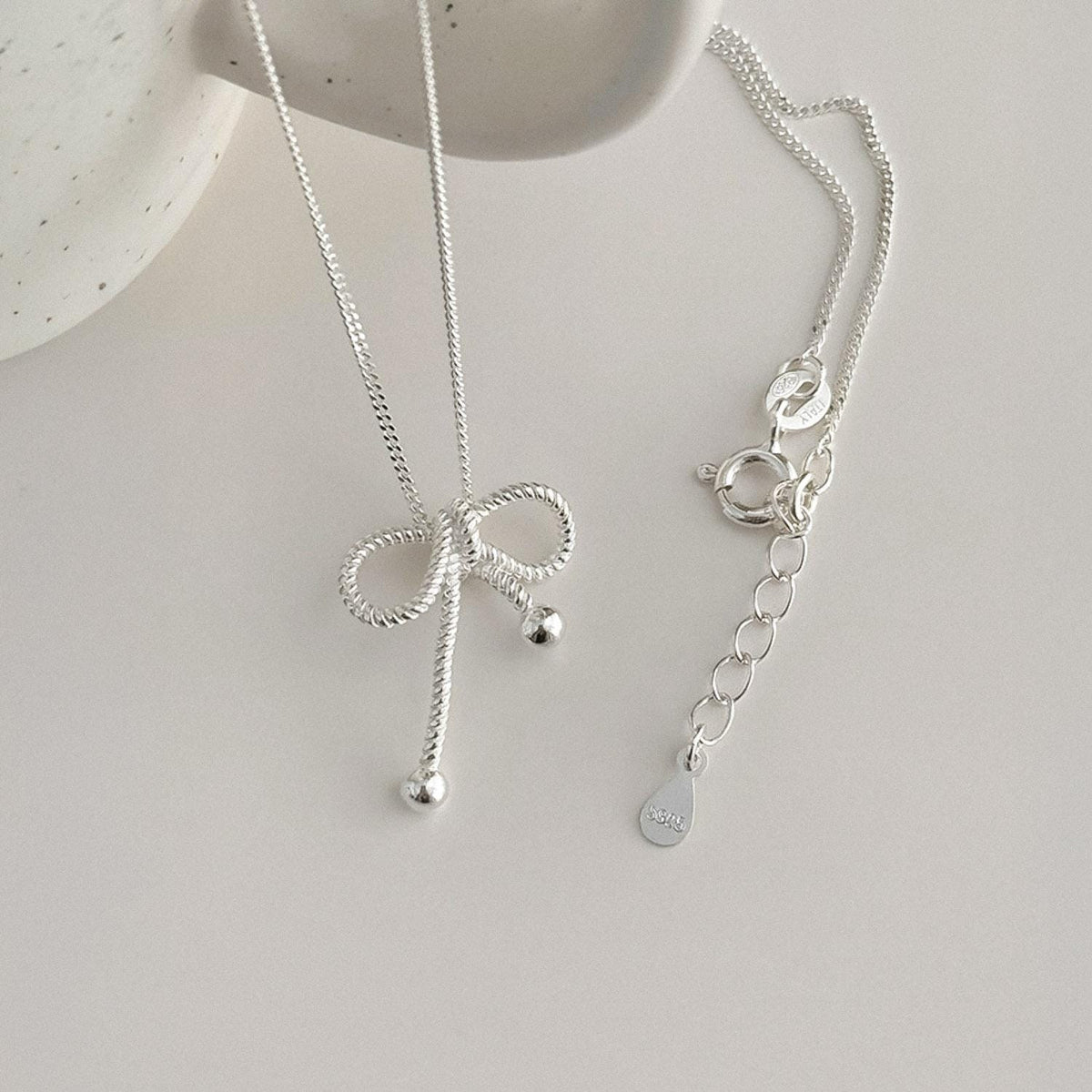 Sterling silver rope bow pendant necklace with delicate ribbon detail on a white background